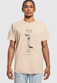 Beige medvilninis marškinėliai su iliustracija ir tekstu „depresso“, kavos tema iliustruotais grafika, trumpomis rankovėmis ir laisvu siluetu.