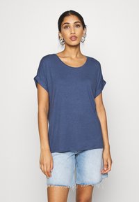 Marineblå kortermet t-skjorte med rund hals og rulleterm, kombinert med lyse denimshorts med frynsete kanter.