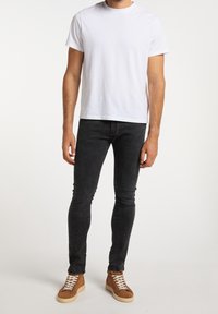 Camiseta de algodón blanca de manga corta, combinada con jeans ajustados negros. Zapatillas marrones con parte superior texturizada y cordones blancos.