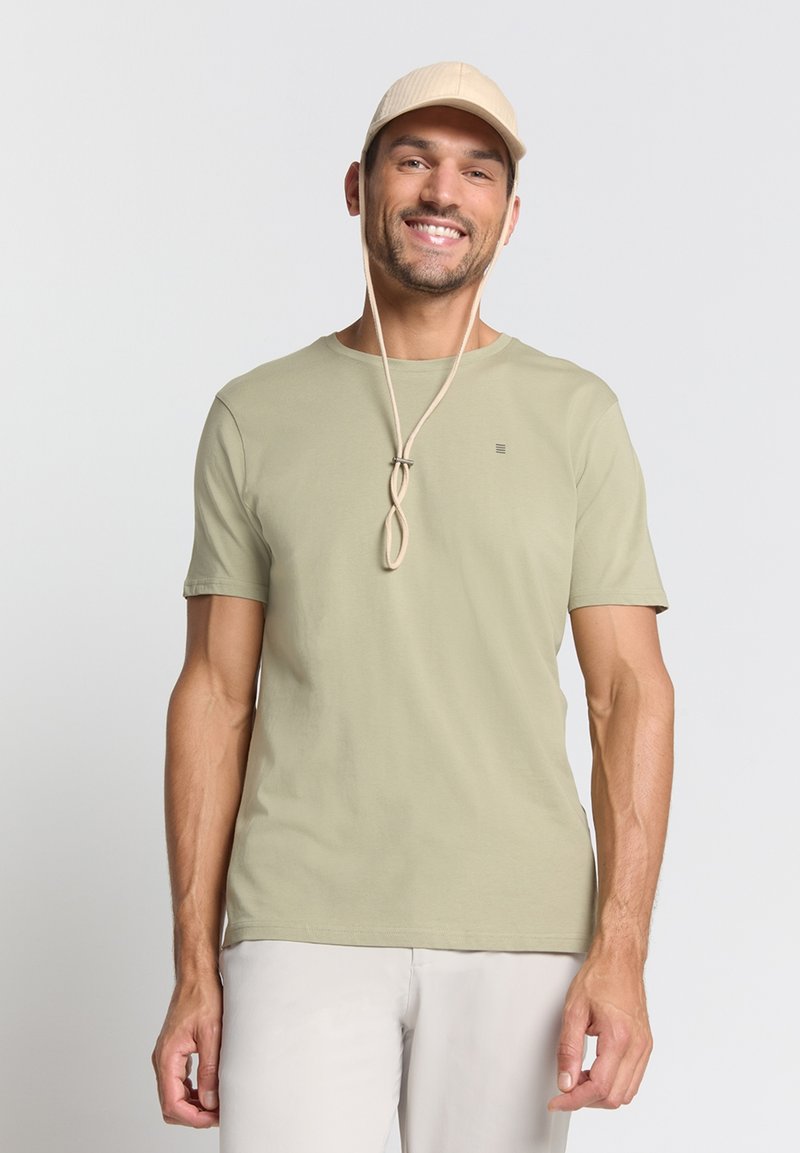 Lichtgroene t-shirt met korte mouwen, ronde halslijn en een subtiele logo. Gecombineerd met een beige pet met een kinband.
