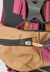 Mochila castanha com padrão de grelha, fecho preto e alças em bordô. Apresenta hardware ajustável e tecido texturizado para melhor aderência.