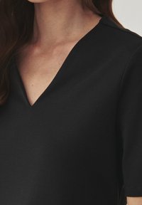 Schwarzes Oberteil mit V-Ausschnitt, kurzen Ärmeln und glatter Textur. Der Stoff wirkt weich und leicht dehnbar.