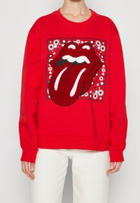 Rotes Sweatshirt mit einem großen Grafikmotiv einer Zunge und Lippen, umgeben von einem Blumenmuster. Hergestellt aus weichem, strukturiertem Stoff mit gerippten Bündchen.