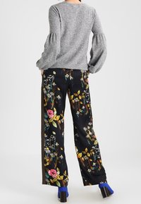Grå puffärmad tröja matchad med svarta vida byxor med färgglada blomstertryck. Modellen bär blå klackskor.