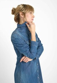 Robe chemise en denim bleu moyen, avec un front à boutons, des manches longues, un col cintré et une coupe décontractée avec des coutures visibles.