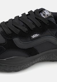 Fekete sneaker textilből és velúrból, fűzőkkel, kontrasztos, texturált oldalsávval, valamint gravírozott logóval a nyelvén és az oldalán.