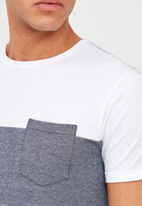 T-skjorte med korte ermer, hvit øvre del og mørkeblå denim-liknende nedre del med en brystlomme. Sirkulært halsdesign.