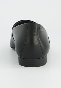 Černá kožená balerína s kulatou špičkou a minimalistickým designem. Má malý logo akcent blízko paty a hladkou texturu.