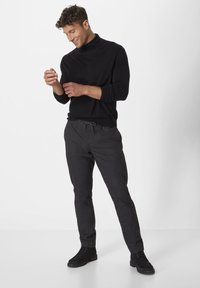 Schwarzer Rollkragenpullover kombiniert mit grauen Jogginghosen und schwarzen Schuhen. Der Pullover hat lange Ärmel und eine figurbetonte Passform.