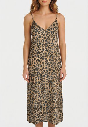 Donna che indossa un abito leopardato senza maniche, lungo fino al ginocchio, con sottili spalline, su sfondo bianco uniforme.