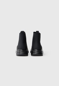 Sorte høj-top sneakers lavet af glat materiale, med en tyk sål og rygstræk, samt diskret branding på siderne.
