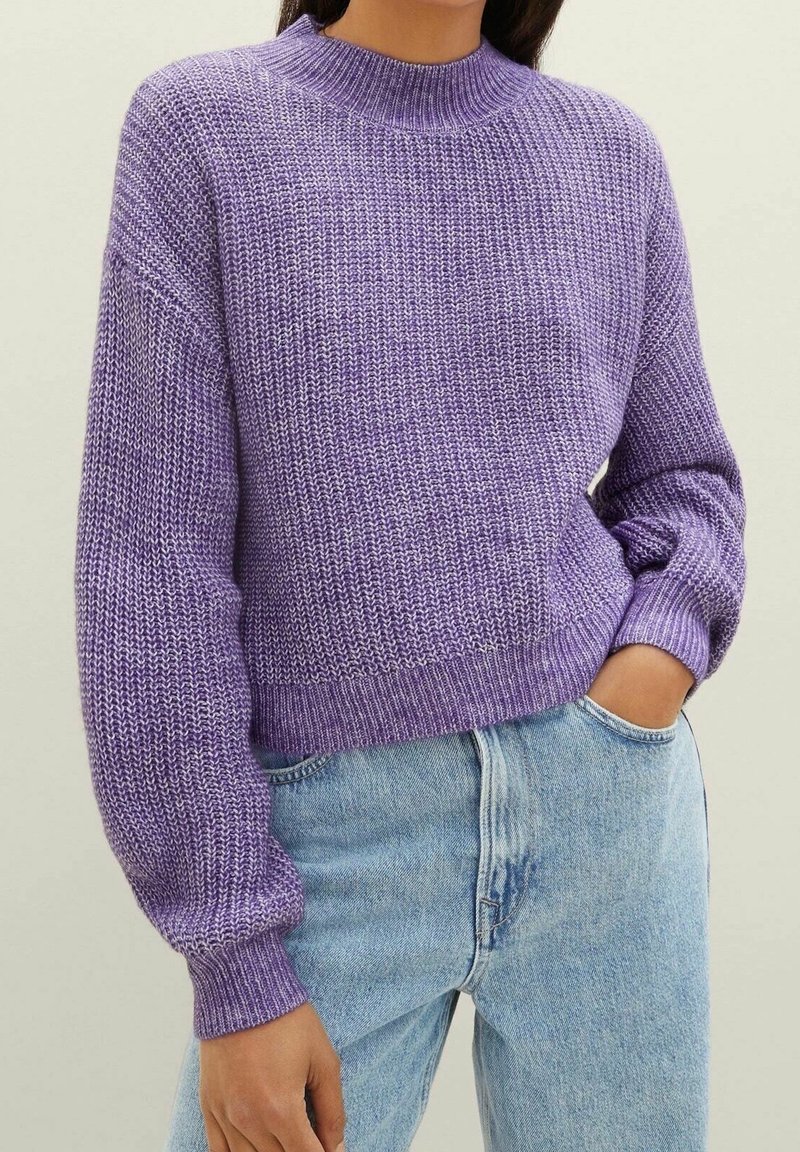 Pull en maille violet avec un col montant, motif structuré, coupe décontractée et poignets côtelés, associé à un jean bleu clair.