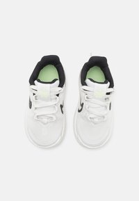 Baskets de sport blanches avec des accents noirs, tige texturée et doublure intérieure verte. Comprend des lacets et un logo sur la languette.