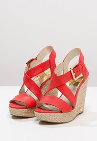 Sandali rossi con zeppa, dotati di cinturini incrociati in tessuto che imitano la tela, con una piattaforma in juta intrecciata e dettagli in metallo dorato.