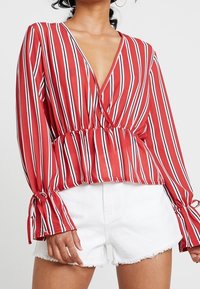 Gestreifte Bluse in Rot und Weiß mit V-Ausschnitt, elastischem Bund und Glockenärmeln. Tragen mit weißen Denim-Shorts mit fransigem Saum.