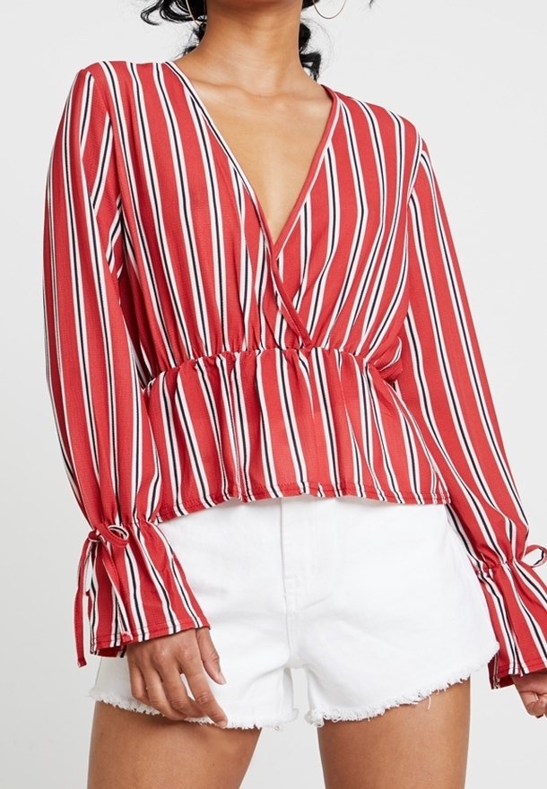 Gestreifte Bluse in Rot und Weiß mit V-Ausschnitt, elastischem Bund und Glockenärmeln. Tragen mit weißen Denim-Shorts mit fransigem Saum.