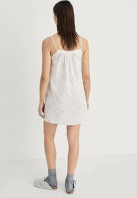 Vestito bianco senza maniche con scollo arricciato e motivo sottile. Indossato con calze grigie e pantofole grigie morbide; lunghezza casual sopra la coscia.