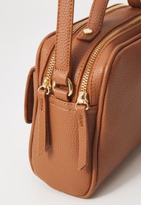 Sac à main en cuir texturé marron avec une forme structurée, fermetures à double zip dorées, et poignées cousues. Comprend des accents en métal doré.