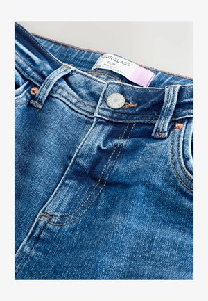 Modré denimové džínsy so slim fit, so zretelným zapínaním na gombík, medenými nitmi a rovnými vreckami. Štítok hovorí "Hourglass Slim."