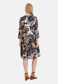 Šaty s květinovým vzorem v námořnické barvě, dlouhé rukávy s kostkovanými manžetami, vrstvený volánový lem a volný střih. Hnědé klínové sandály.