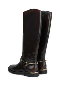 Botas de goma burdeos brillantes hasta la rodilla, con punta redonda, detalle en tira negra y acentos en tono dorado en el talón y herrajes de la tira.