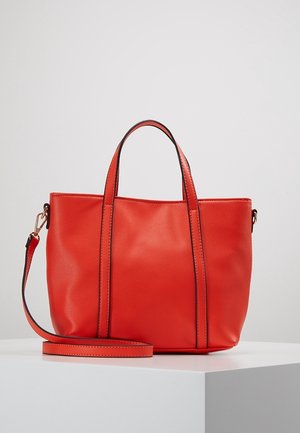 Rode leren tas met twee handvatten en een afneembare schouderriem, tentoongesteld op een wit platform tegen een effen achtergrond.