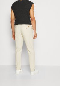 Maglione a maniche corte grigio scuro in maglia abbinato a pantaloni beige chiaro. I pantaloni presentano tasche posteriori con bottoni e un dettaglio di tasca laterale.
