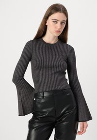 Grijze geribbelde langemouwen shirt met een aansluitend lichaam en uitlopende mouwen, gemaakt van een textuurmateriaal. Gecombineerd met hooggerokte zwarte leren broek.