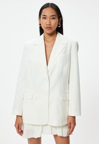 Witte op maat gemaakte blazer met een enkelvoudig ontwerp, normale revers en twee voorzakken. Zachte stof met een gladde textuur, minimale details.