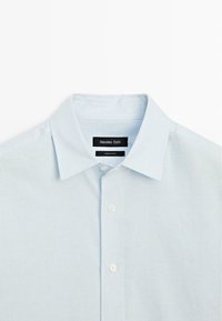 Camicia a righe azzurro chiaro con collo button-down, con bottoni bianchi e etichetta con la scritta "Massimo Dutti". Prodotta in Cina.