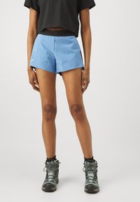 Lyseblå treningsshorts laget av lett stoff med en svart livlinje, kombinert med mønstrede tursko med grå og teal detaljer.