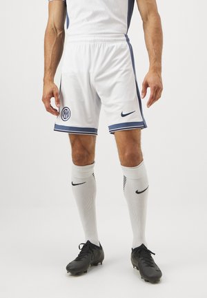 Hvide fodboldshorts med blå accenter og et emblem, parret med hvide strømper med et sort logo og sorte fodboldstøvler.