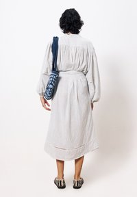 Helles grau gestreiftes Kleid mit puffärmel, tailliert und knielang. Kombiniert mit einer aufwendigen blauen Häkelhandtasche und gemustertem Schuhwerk.