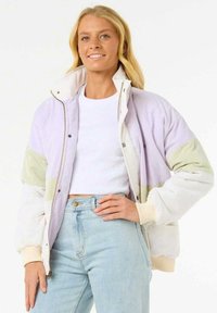 Giacca imbottita in lavanda, bianco e verde chiaro. Presenta una chiusura con zip, polsini a costine e una vestibilità rilassata. Indossata sopra una maglietta bianca.