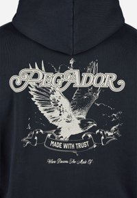 Marineblå hoodie med et stort grafik af en ørn med spredte vinger, hvid tekst "PEGADOR" og "MADE WITH TRUST" på et banner nedenunder.