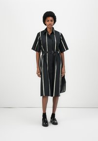 Rochie cămașă cu dungi negre și linii verticale albe, cu mâneci scurte, cu curea la talie, până la gambe, și cu o despicătură pe o parte.