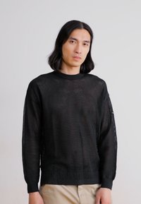 Black knit sweater with a loose, open weave. Features long sleeves, a rounded neckline, and ribbed cuffs and hem.