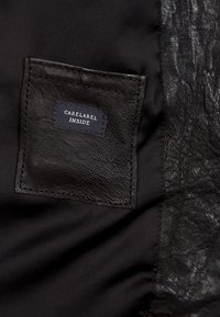 Czarna tkanina z teksturowaną skórzaną naszywką z białą metką pielęgnacyjną z napisem „CARELABEL INSIDE”. Widoczne gładkie, ciemne tło.