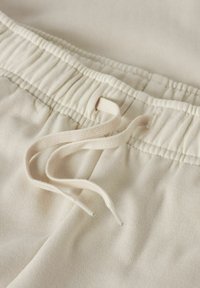 Povečava bež elastičnega pasu z vrvico iz blaga na mehkih bombažnih hlačah ali kratkih hlačah.