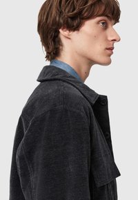 Černá džínová bunda s límečkem, zapínáním na knoflíky a boční kapsou na hrudi. Tkanina má texturovaný povrch.