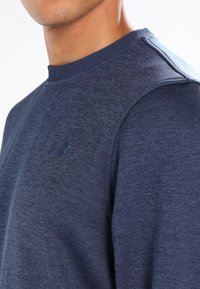 Felpa blu navy con tessuto strutturato, collo a coste girocollo e accenti sulle spalle. Presenta un logo discreto sul petto.