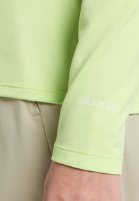 Camicia verde lime a maniche lunghe realizzata in tessuto testurizzato; presenta un logo bianco "TEXADRI" sulla manica e dettagli di cucitura nei polsini.