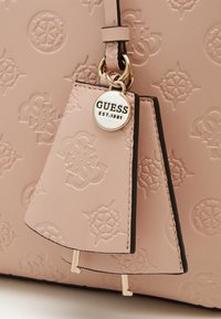 Poskipuna vaaleanpunainen käsilaukku, joka on valmistettu kohokuvioidusta keinonahasta ja jossa on logokuvio sekä metallinen tunniste. Laukussa on kullanväriset metalliosat ja litteä tunniste, joissa on nahkaiset yksityiskohdat.