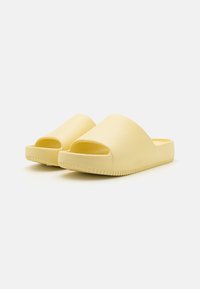 Gule slip-on sko med åpen tå, glatt tekstur, buet design og rillede gummisåler. Minimalistisk stil uten ekstra utsmykninger.