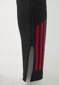 Schwarze sportliche Shorts mit roten vertikalen Streifen, ausgestattet mit einem seitlichen Reißverschluss zur Anpassung und einem strukturierten Stoffeinsatz.