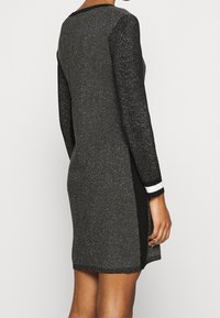 Robe en maille noire et grise à manches longues, tissu texturé, léger scintillement, et rayures blanches contrastantes aux poignets des manches.