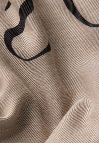 Gros plan sur un tissu beige texturé avec des lignes courbes noires et des plis doux créant des ombres et des reflets.