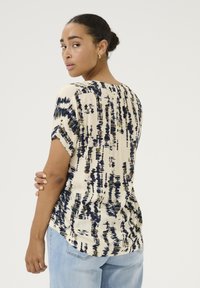 Blouse �à manches courtes en crème avec un motif abstrait bleu marine et olive. Tissu léger, ourlet arrondi et coupe décontractée. Vue de dos montrée.