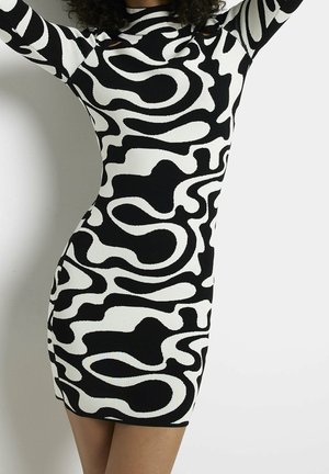 Eng anliegendes schwarz-weißes Kleid mit abstraktem Muster und langen Ärmeln, getragen von einer Person mit lockigem Haar, die die Arme über dem Kopf erhoben hat.