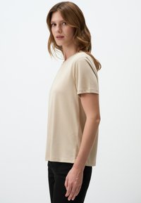 Beige t-shirt met korte mouwen en een ronde halslijn, gemaakt van een soepele stof, met een relaxte pasvorm en zijnaden voor structuur.
